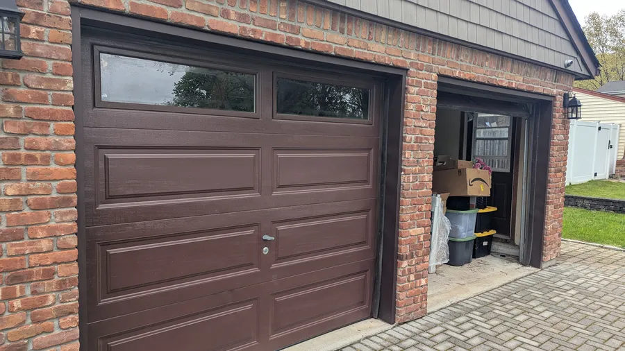 Two matching brown raised-panel garage doors with windows installed on a Long Island, NY brick home