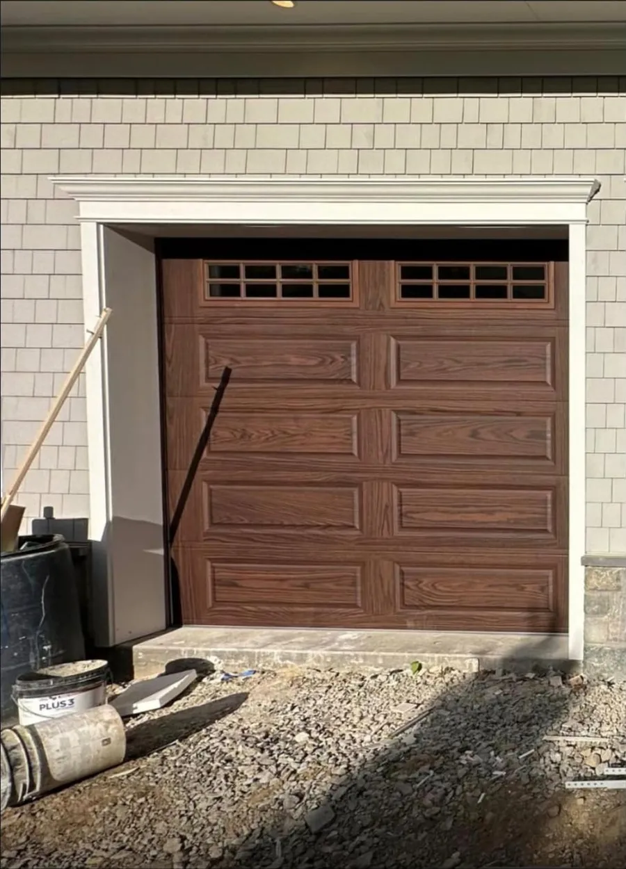 Newly installed wood-grain steel raised-panel garage door with a row of insulated windows on a Queens, NY home